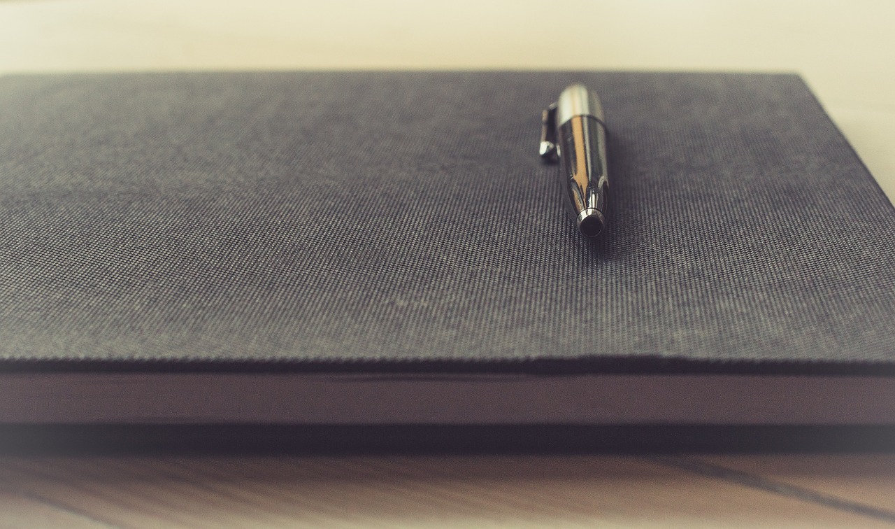 A pen sits on a closed book containing content ideas for an editorial calendar. 