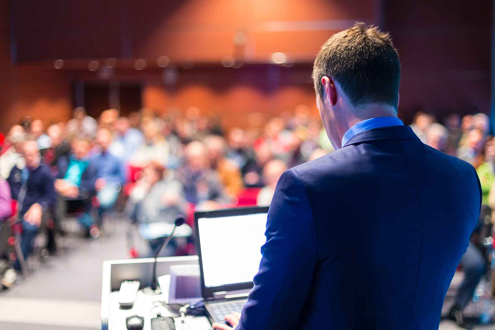A man stands in front of a crowd, delivering a presentation, symbolising speech writing services.