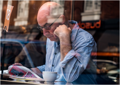 A man reading a newspaper, with a coffee.