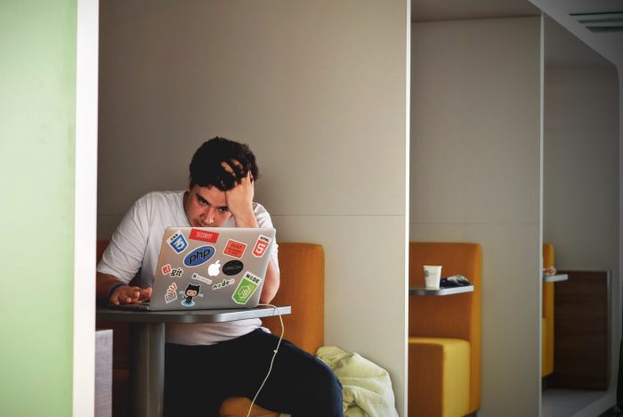 A young man looking stressed, over his laptop.