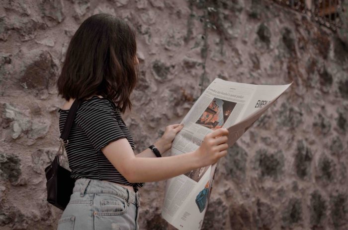 A young woman reading a newspaper with attention grabbing headlines.